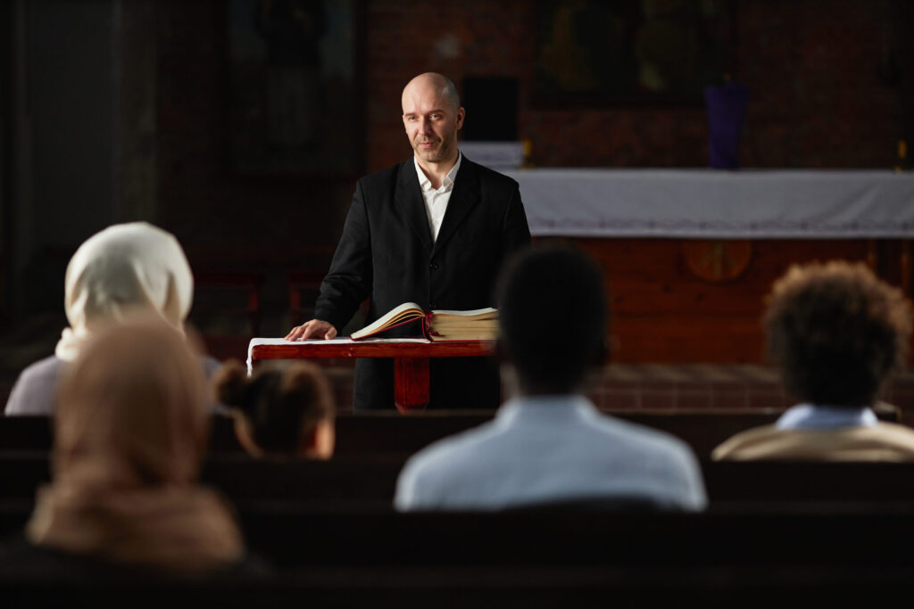 Mature preacher standing at altar with Bible and reading prayer for people in church
